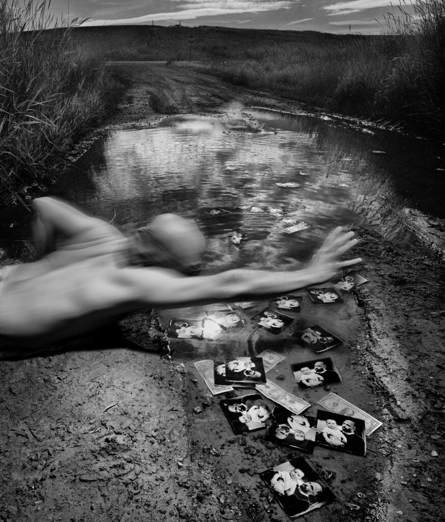 Black and white photograph of a man diving in a pool with photos and cash on the bottom