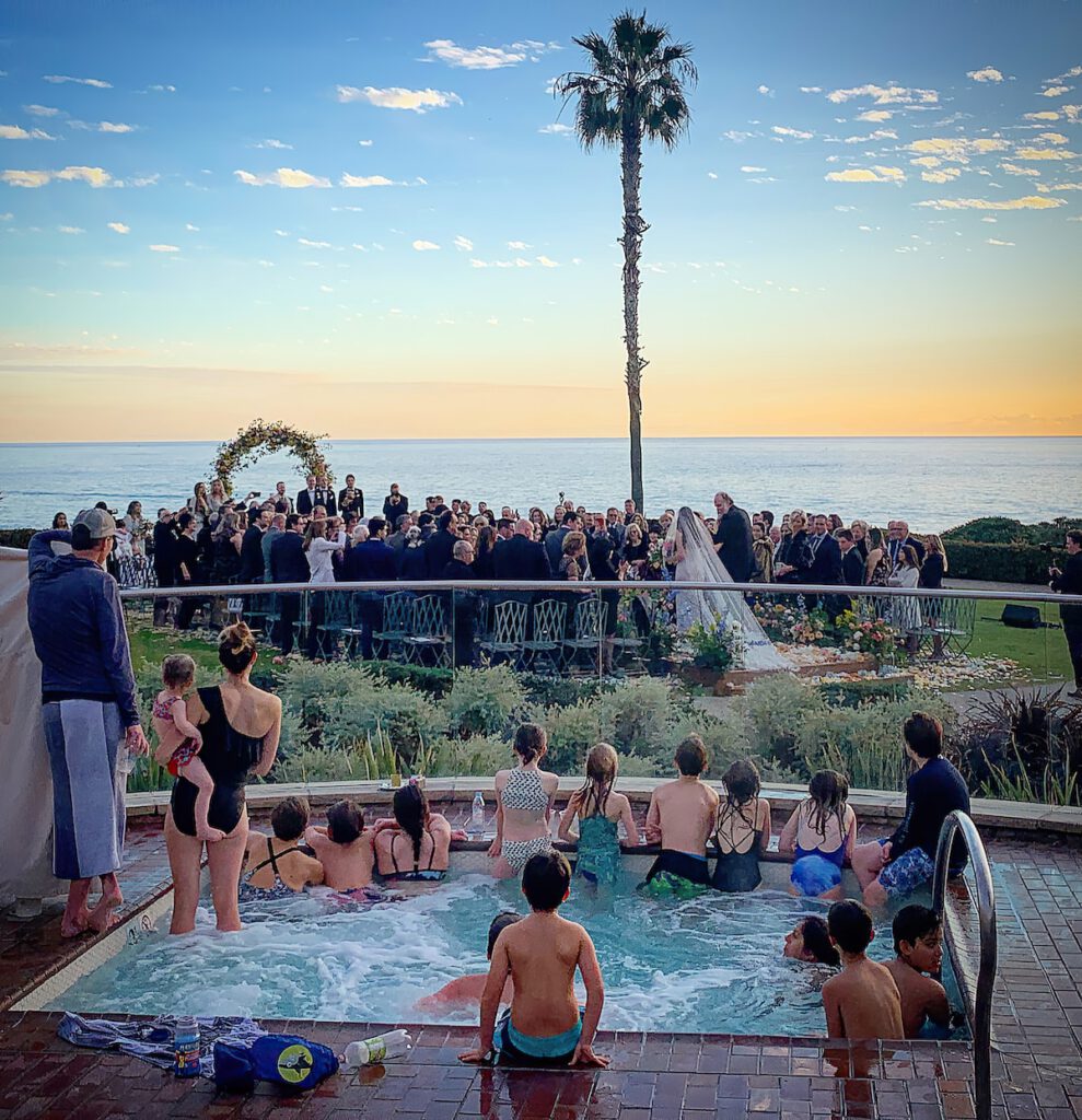 A color photograph with dozens of people in the foreground watching a formal wedding