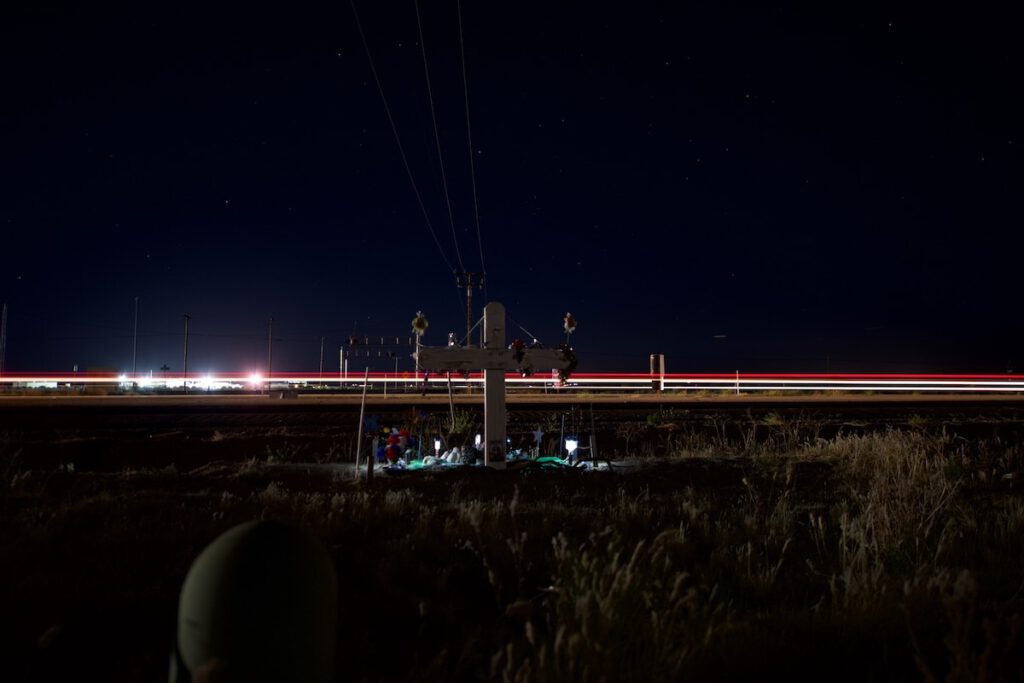 Nighttime photograph of a cross with lit candles on the side of a busy road