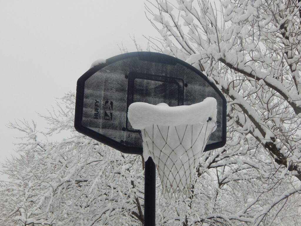 Black and white photograph of a basketball hoop covered with snow