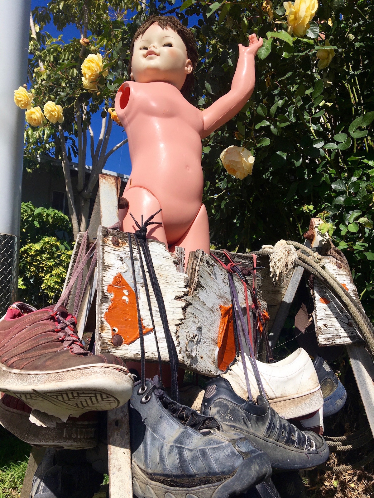 naked plastic doll on top of an old birch birdhouse with shoes hung up on it